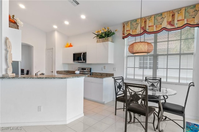 kitchen featuring white cabinetry, appliances with stainless steel finishes, dark stone counters, and kitchen peninsula