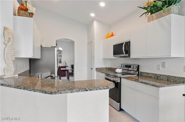 kitchen with dark stone countertops, kitchen peninsula, white cabinets, and appliances with stainless steel finishes