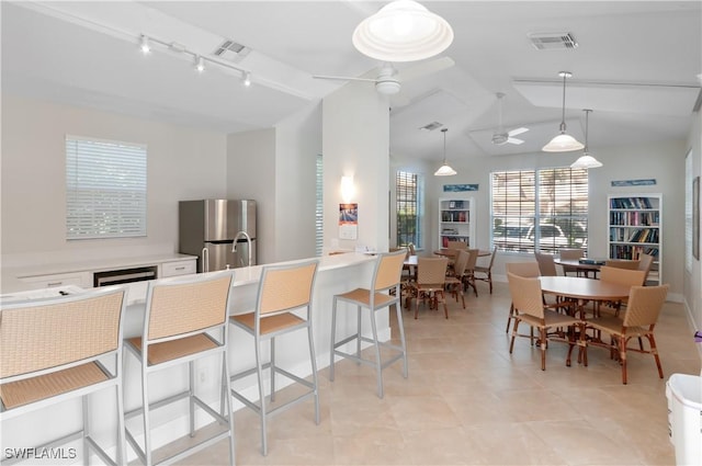 kitchen featuring stainless steel fridge, a breakfast bar area, ceiling fan, white cabinets, and decorative light fixtures