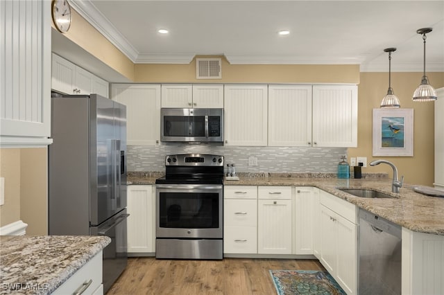 kitchen with appliances with stainless steel finishes, white cabinetry, sink, crown molding, and light stone countertops