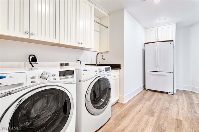 laundry room featuring cabinets, sink, washing machine and dryer, and light hardwood / wood-style flooring