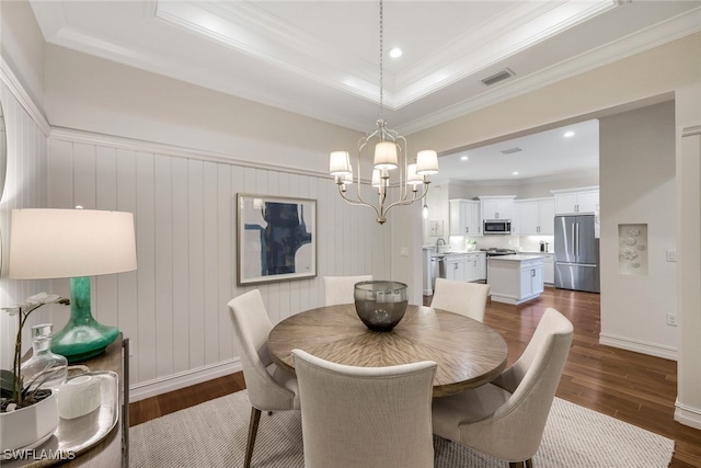 dining area with a raised ceiling, ornamental molding, dark hardwood / wood-style floors, and an inviting chandelier