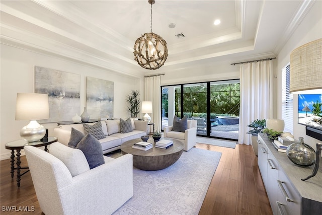 living room featuring crown molding, a tray ceiling, wood-type flooring, and an inviting chandelier