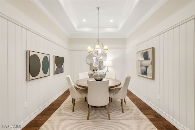 dining space with a raised ceiling, crown molding, hardwood / wood-style floors, and an inviting chandelier