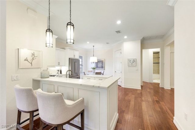 kitchen with stainless steel refrigerator, a breakfast bar, white cabinetry, decorative light fixtures, and kitchen peninsula