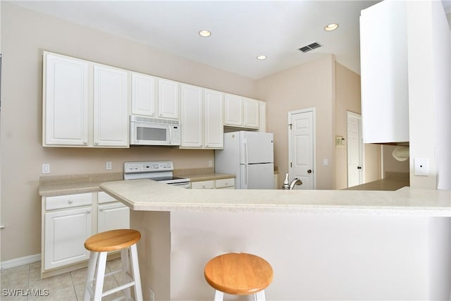 kitchen with a kitchen bar, white cabinetry, light tile patterned floors, kitchen peninsula, and white appliances