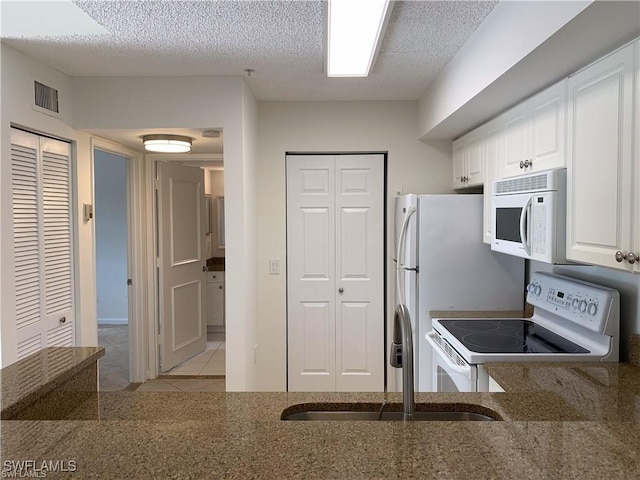 kitchen featuring sink, white appliances, light tile patterned floors, a textured ceiling, and white cabinets