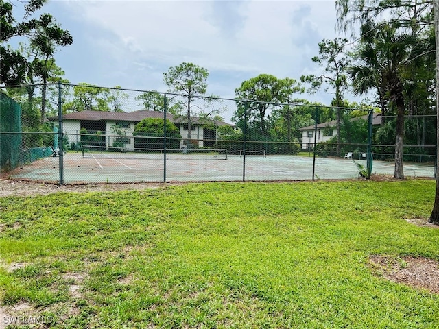 view of tennis court with fence and a yard