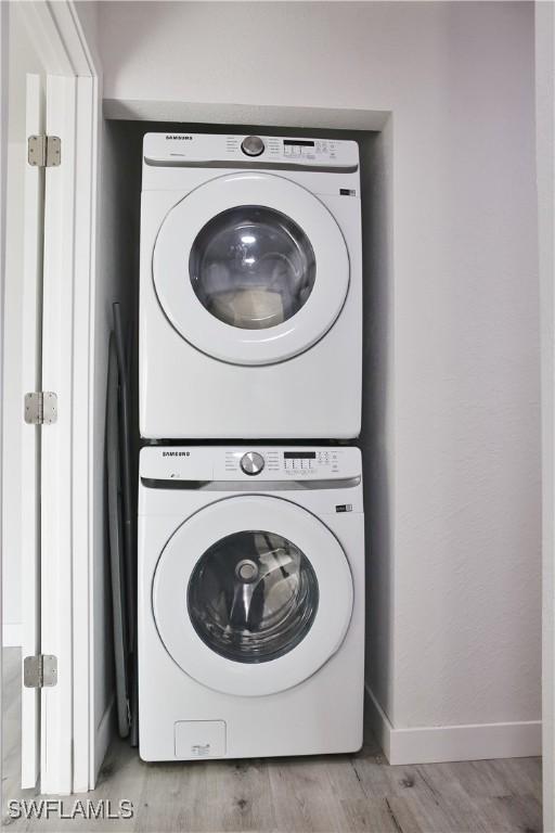 laundry area with light wood-type flooring and stacked washer / dryer