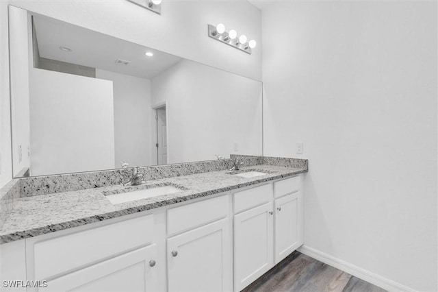 full bath with double vanity, wood finished floors, a sink, and baseboards