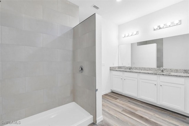 full bath with double vanity, visible vents, wood finished floors, a tile shower, and a sink