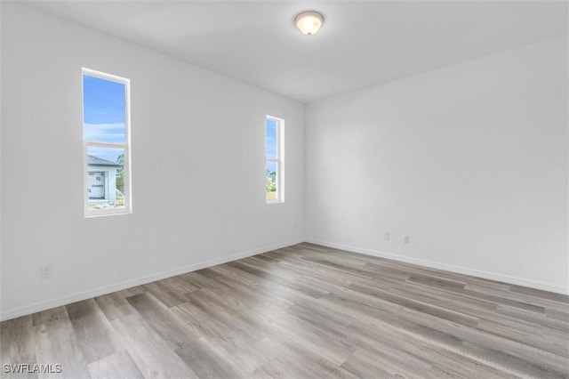 spare room with wood finished floors, a wealth of natural light, and baseboards