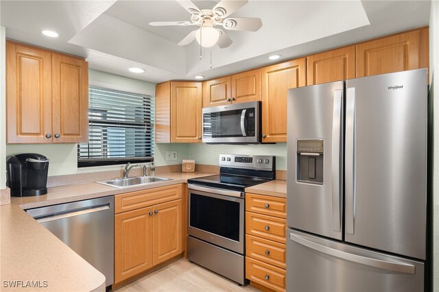 kitchen with ceiling fan, appliances with stainless steel finishes, a tray ceiling, and sink