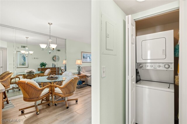 washroom featuring stacked washer / drying machine, a notable chandelier, light hardwood / wood-style floors, and electric panel