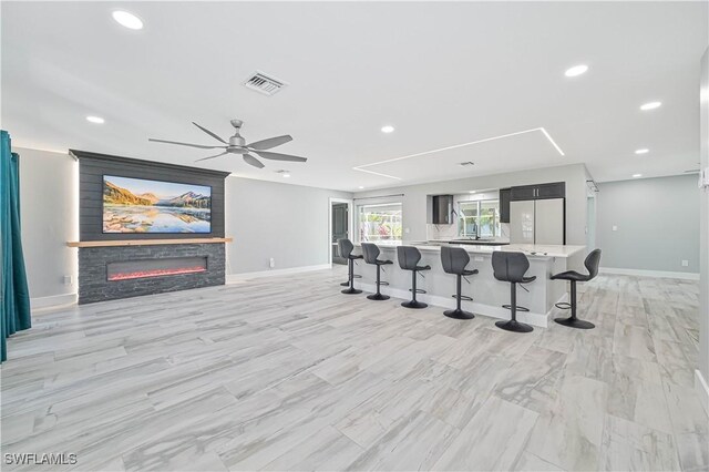 interior space with a large island, ceiling fan, a fireplace, a kitchen bar, and white fridge