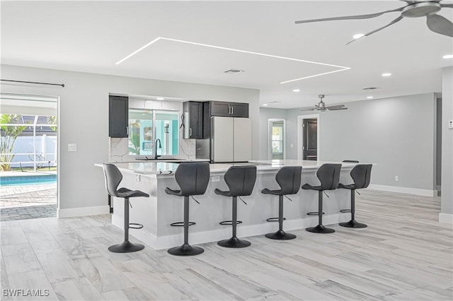 kitchen featuring sink, a kitchen bar, decorative backsplash, white fridge, and a large island