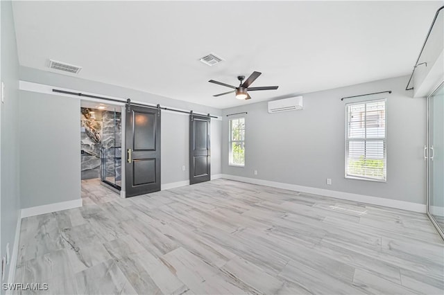 unfurnished bedroom with ceiling fan, a wall mounted air conditioner, a barn door, and multiple windows