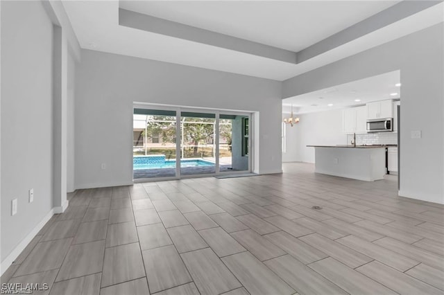 unfurnished living room with a tray ceiling and a chandelier