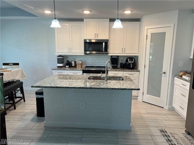 kitchen featuring pendant lighting, sink, white cabinetry, stainless steel appliances, and an island with sink