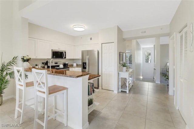 kitchen with light tile patterned floors, appliances with stainless steel finishes, white cabinetry, kitchen peninsula, and dark stone counters