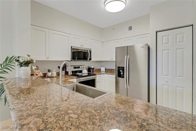 kitchen with stainless steel appliances, white cabinetry, stone counters, and kitchen peninsula