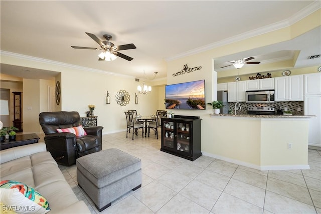 living room with light tile patterned floors, ornamental molding, ceiling fan with notable chandelier, and baseboards