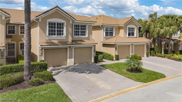 view of property with an attached garage, a tiled roof, decorative driveway, and stucco siding