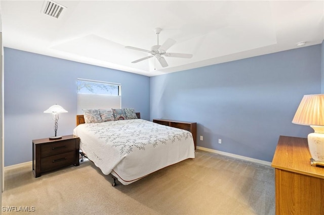 bedroom with light carpet, a tray ceiling, visible vents, and baseboards