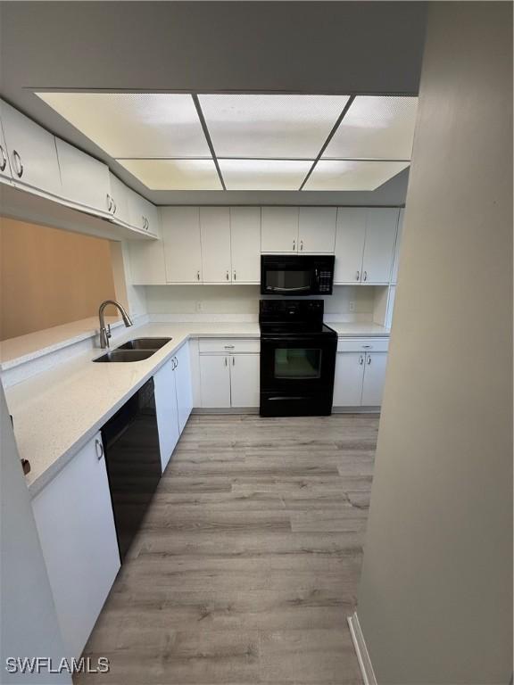 kitchen with white cabinetry, sink, light hardwood / wood-style flooring, and black appliances