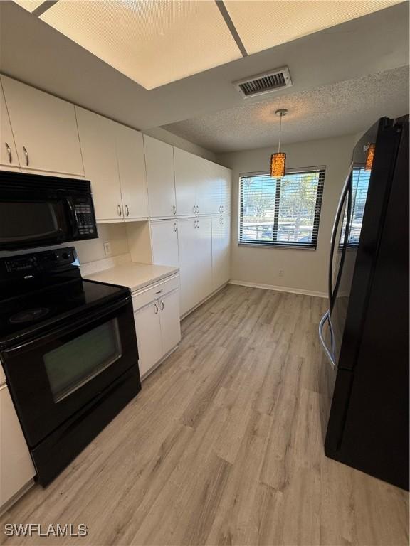 kitchen featuring pendant lighting, white cabinetry, black appliances, a textured ceiling, and light hardwood / wood-style flooring