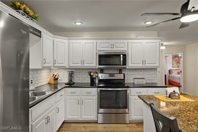 kitchen with sink, appliances with stainless steel finishes, white cabinetry, light hardwood / wood-style floors, and decorative backsplash