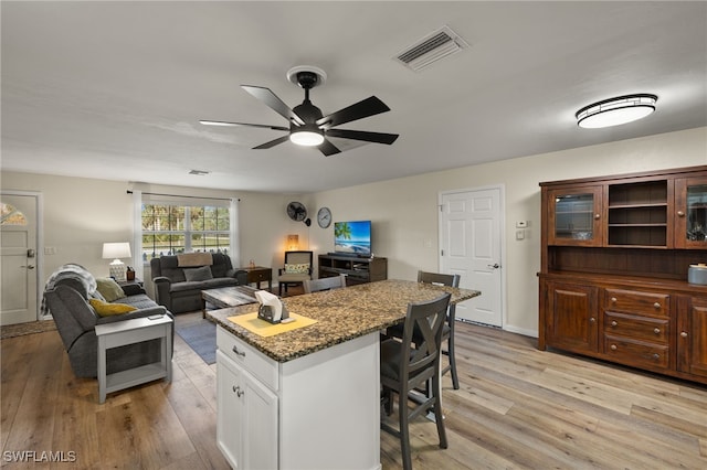 kitchen with white cabinetry, dark stone counters, a kitchen bar, and light hardwood / wood-style flooring