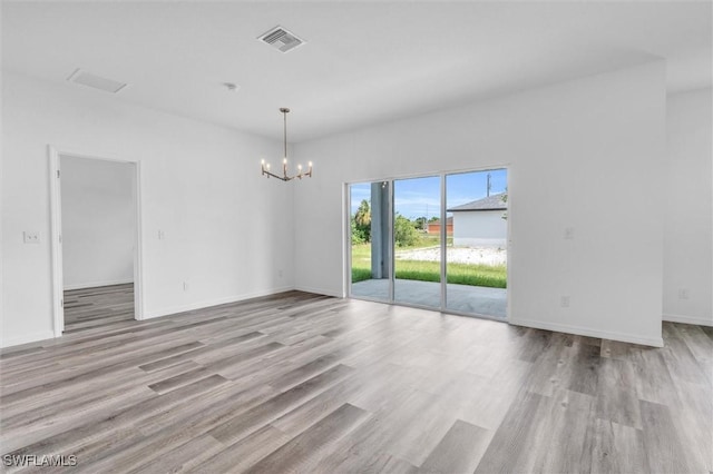 unfurnished room with visible vents, a notable chandelier, baseboards, and wood finished floors