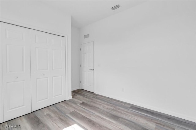 unfurnished bedroom with baseboards, a closet, visible vents, and wood finished floors