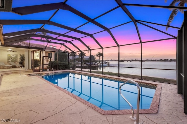 pool at dusk with a lanai, a patio, ceiling fan, and a water view