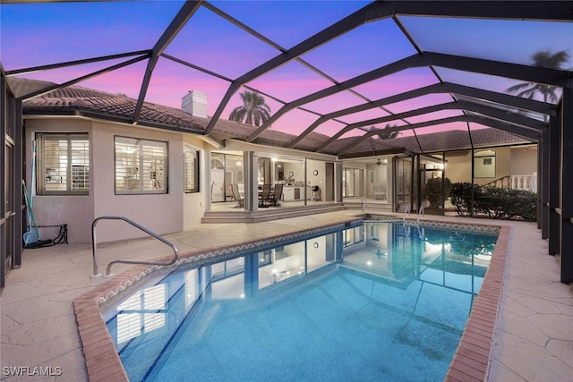 pool at dusk with a patio and glass enclosure