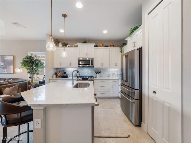 kitchen with stainless steel appliances, an island with sink, white cabinets, and decorative light fixtures