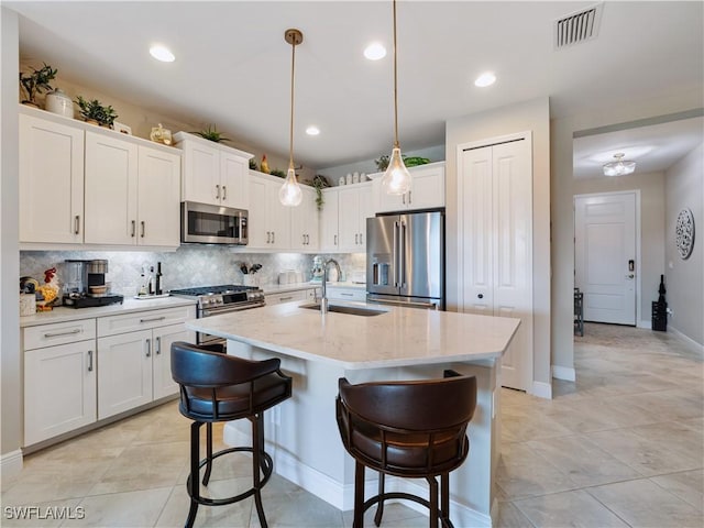 kitchen with sink, hanging light fixtures, a center island with sink, appliances with stainless steel finishes, and white cabinets