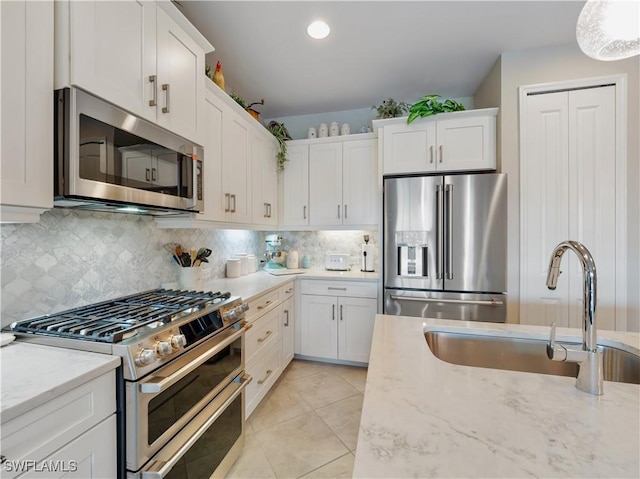 kitchen with sink, appliances with stainless steel finishes, white cabinetry, light stone counters, and decorative backsplash