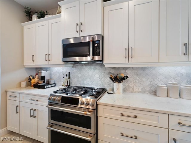 kitchen with appliances with stainless steel finishes, backsplash, white cabinets, and light stone counters