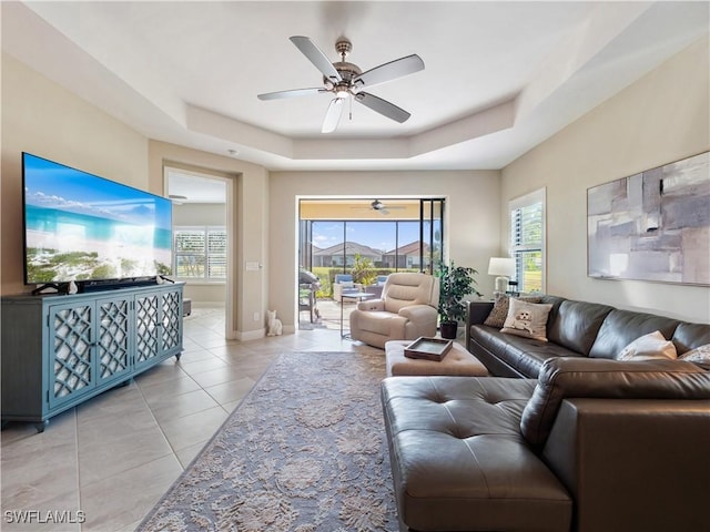 tiled living room with ceiling fan and a raised ceiling