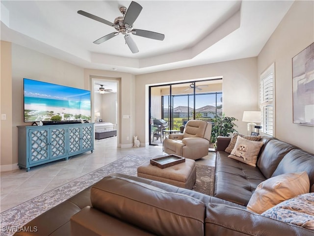 living room with a raised ceiling, light tile patterned floors, and ceiling fan