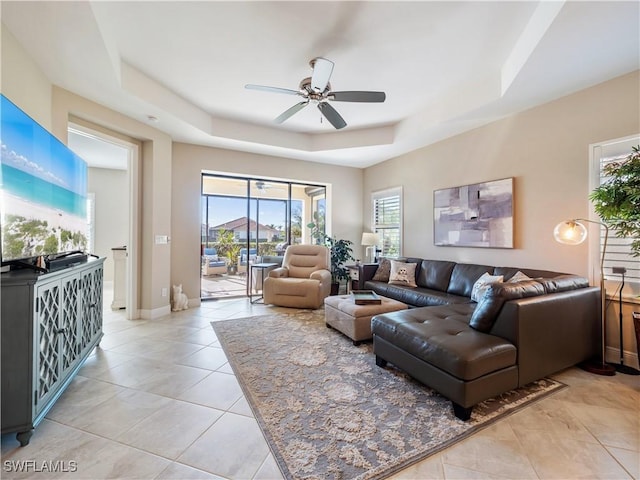 tiled living room with a raised ceiling and ceiling fan