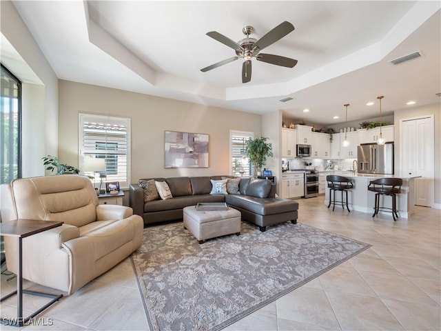 tiled living room with a raised ceiling, sink, and a wealth of natural light