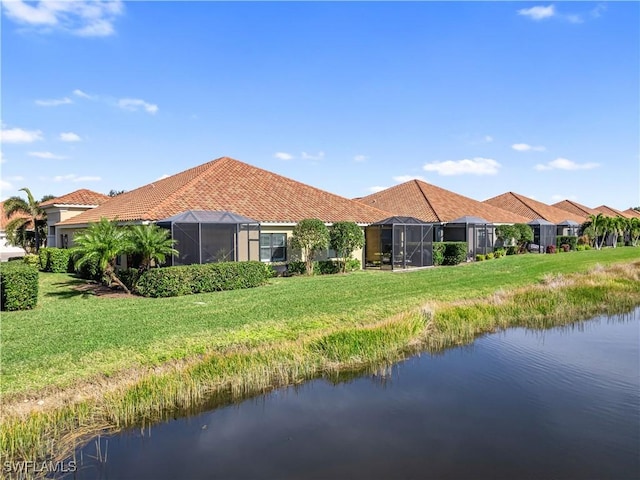 back of property with a yard, a water view, and glass enclosure