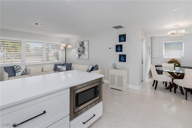 kitchen featuring stainless steel microwave, a notable chandelier, and white cabinets