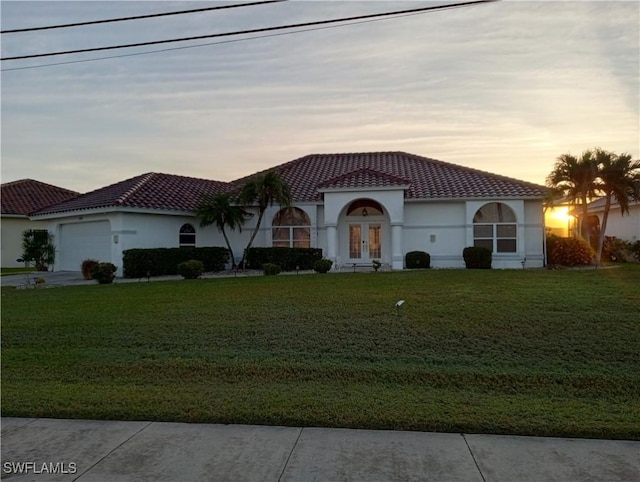 mediterranean / spanish-style house with a garage, a yard, and french doors