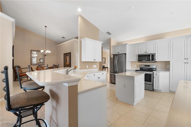 kitchen with appliances with stainless steel finishes, white cabinets, decorative light fixtures, vaulted ceiling, and kitchen peninsula