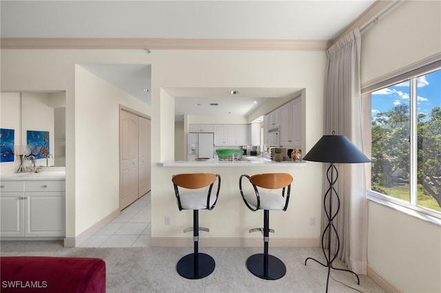 kitchen with light tile patterned floors, ornamental molding, a kitchen breakfast bar, white appliances, and white cabinets