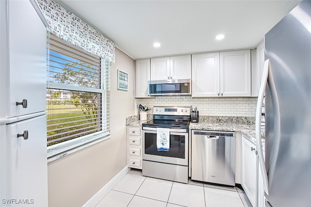 kitchen featuring tasteful backsplash, light stone counters, white cabinets, and appliances with stainless steel finishes